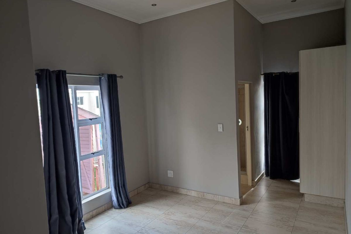A bright bedroom featuring neutral wall tones, tiled flooring, recessed ceiling lighting, and a built-in wardrobe with an adjacent en-suite bathroom entrance.