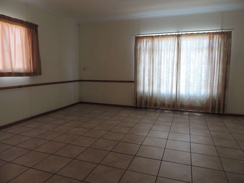 A spacious, empty living area featuring neutral ceramic floor tiles and a decorative wooden dado rail, offering a blank canvas for interior design.