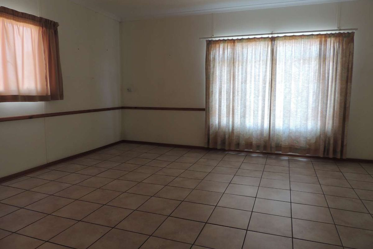 A spacious, empty living area featuring neutral ceramic floor tiles and a decorative wooden dado rail, offering a blank canvas for interior design.