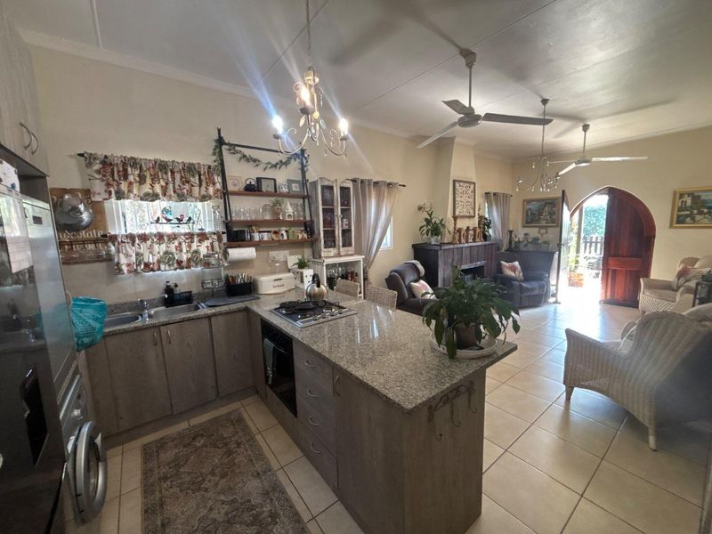 Open-plan kitchen and living area featuring granite countertops, built-in appliances, tiled flooring, and an arched entrance leading to the exterior.