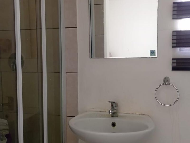 A functional bathroom featuring a pedestal basin, wall-mounted mirror, and a glass-enclosed shower stall with tiled walls.
