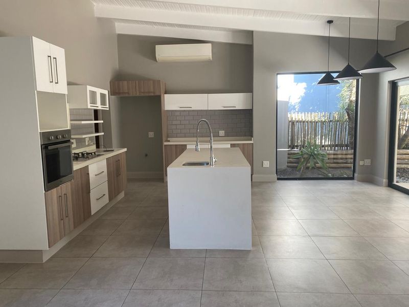 Modern open-plan kitchen featuring a central island, built-in oven, gas hob, subway tile backsplash, and large windows overlooking the garden.
