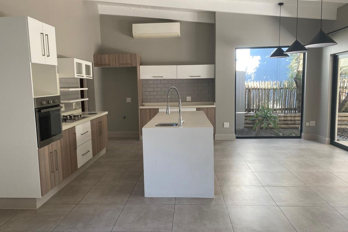 Modern open-plan kitchen featuring a central island, built-in oven, gas hob, subway tile backsplash, and large windows overlooking the garden.