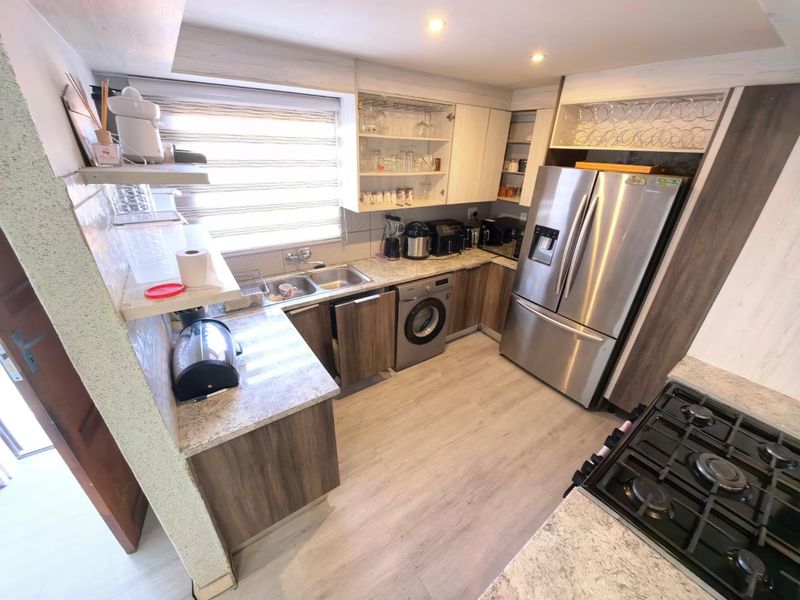 A functional kitchen featuring stone countertops, built-in cabinetry, a gas hob, and integrated laundry facilities, offering a practical and well-organized workspace.