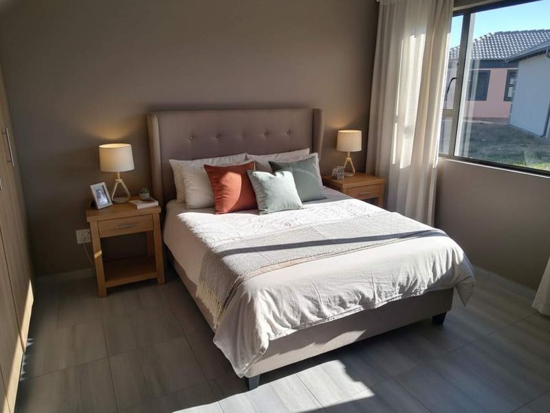 A well-lit bedroom featuring neutral wall tones, tiled flooring, and a built-in wardrobe, offering a comfortable and functional living space.