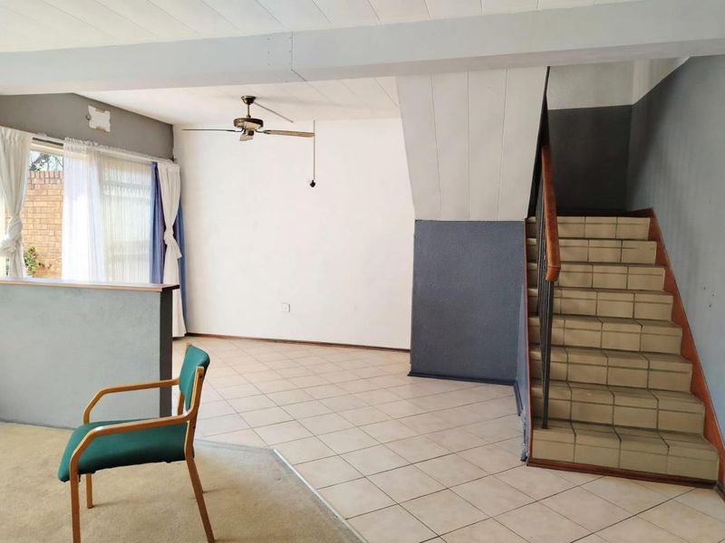 Spacious living area featuring ceramic floor tiles, a staircase with a metal handrail, and a ceiling fan, offering a blank canvas for renovation.