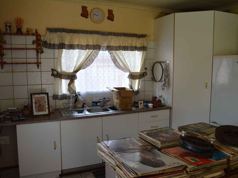 A dated kitchen featuring original cabinetry, a stainless steel sink, and tiled backsplash, offering significant potential for a modern renovation.