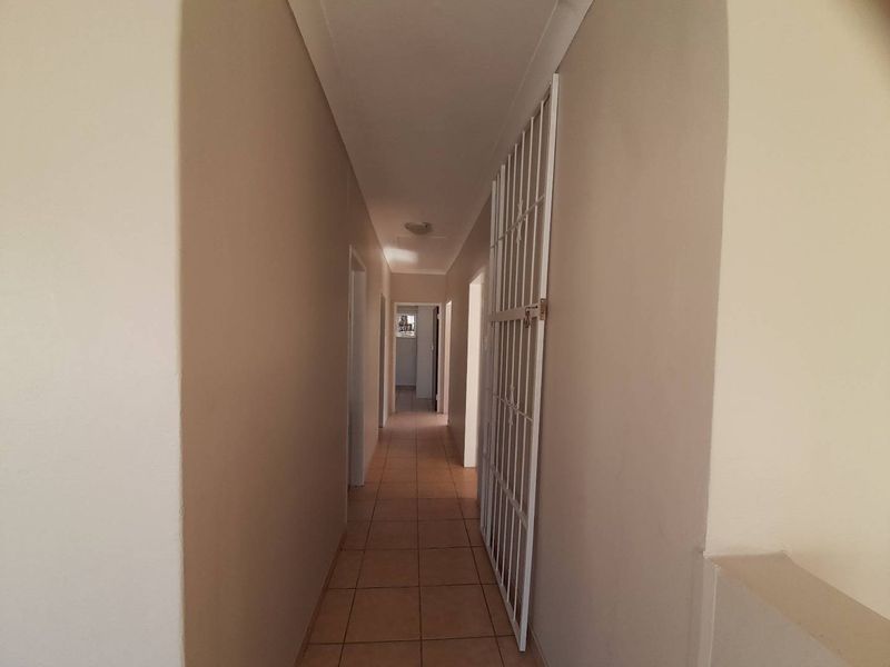 A clean, neutral-toned hallway featuring tiled flooring and a fitted security gate, providing access to multiple rooms within the home.