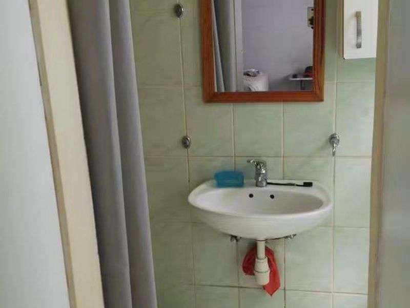 A compact bathroom featuring a wall-mounted basin, tiled walls and flooring, and a wall-mounted mirror and cabinet.