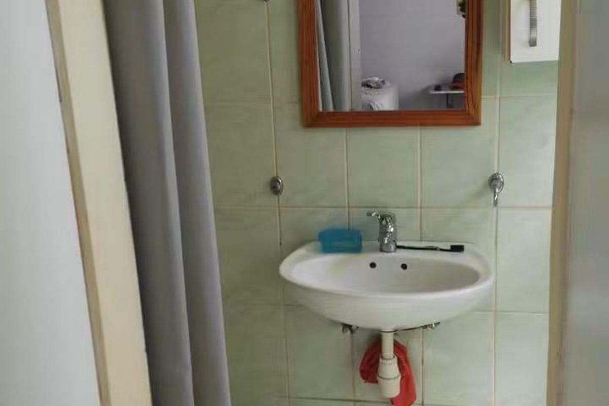 A compact bathroom featuring a wall-mounted basin, tiled walls and flooring, and a wall-mounted mirror and cabinet.