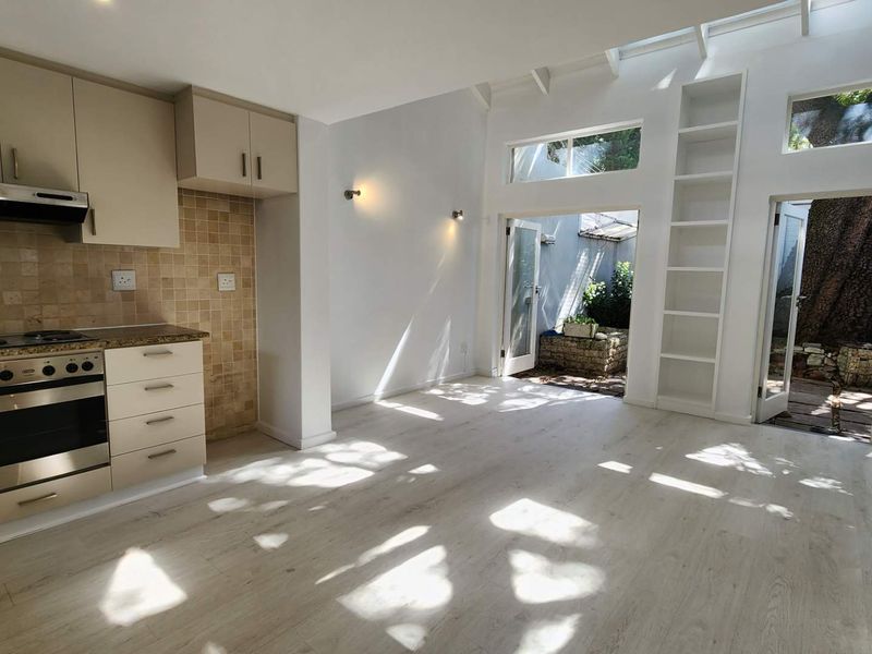 Bright open-plan kitchen and living area featuring modern cabinetry, built-in appliances, laminate flooring, and double doors leading to a private outdoor space.