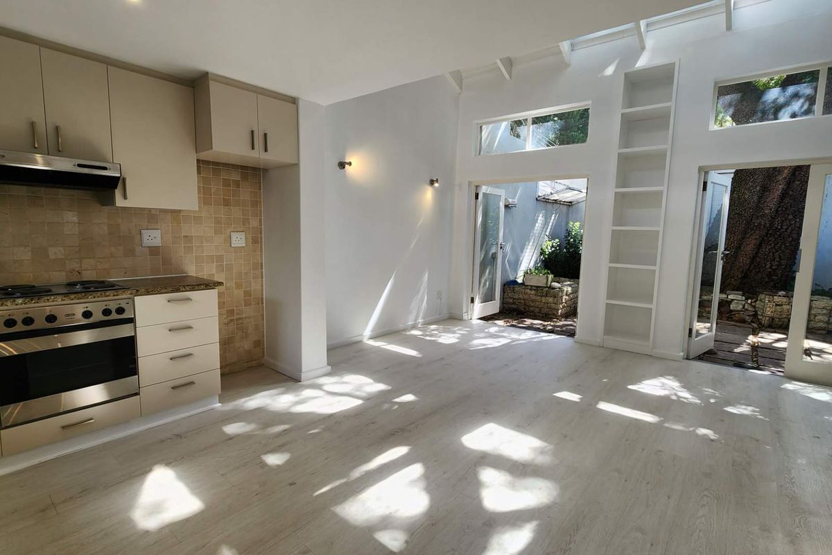 Bright open-plan kitchen and living area featuring modern cabinetry, built-in appliances, laminate flooring, and double doors leading to a private outdoor space.