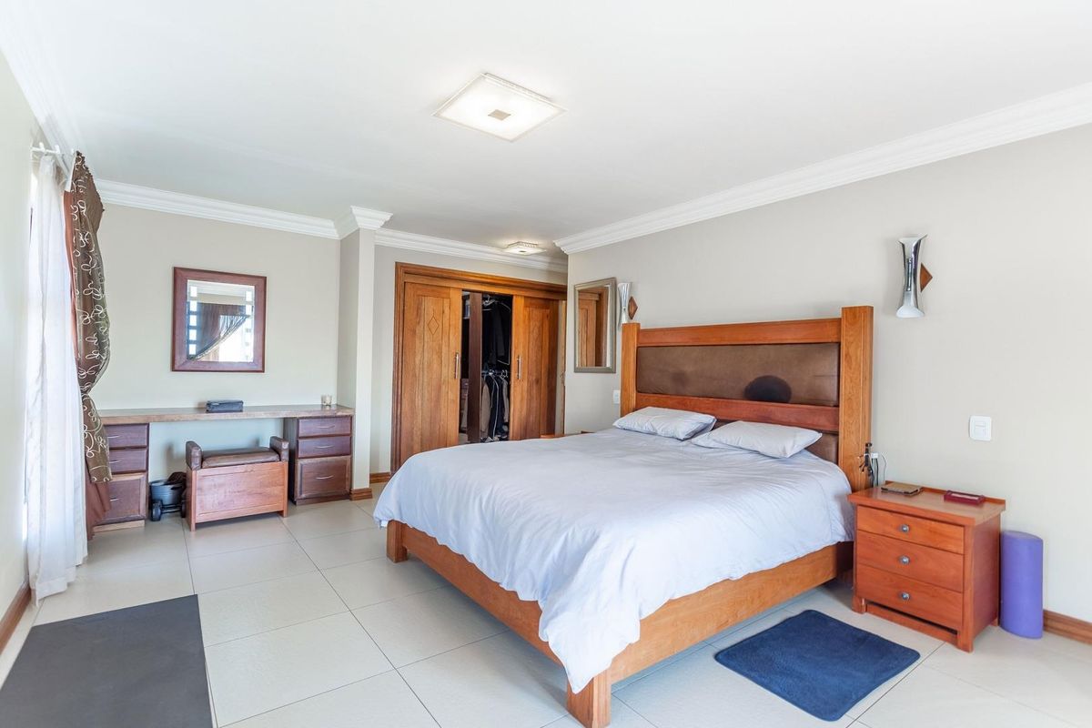 Spacious bedroom featuring built-in wooden cabinetry, tiled flooring, crown molding, and wall-mounted lighting fixtures.