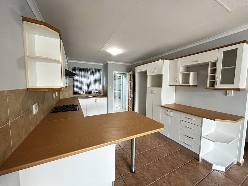A functional kitchen featuring white cabinetry, wood-look laminate countertops, a gas hob, and tiled flooring, offering a clean and practical workspace.