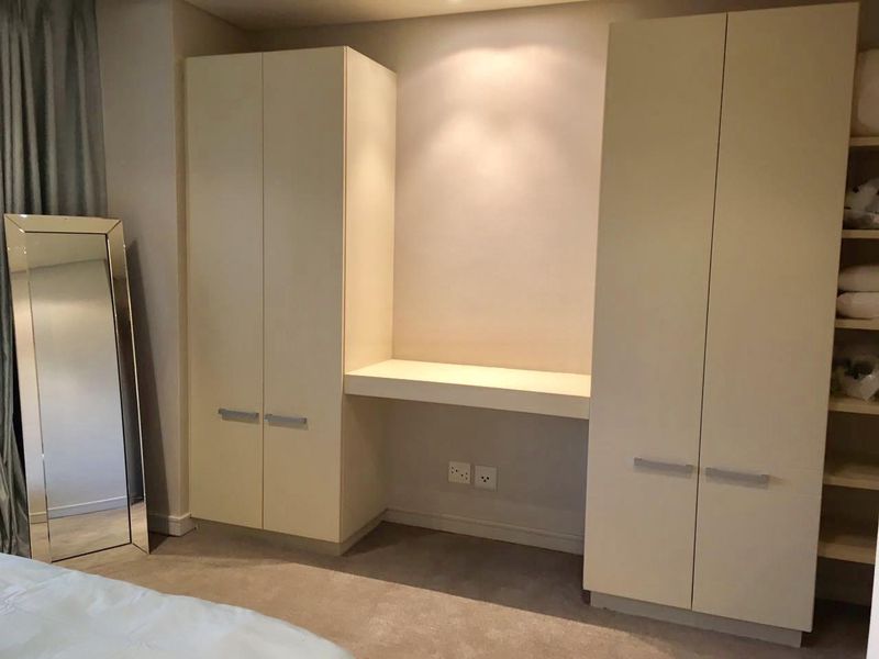 A well-maintained bedroom featuring custom built-in wardrobes with an integrated desk area and neutral finishes.