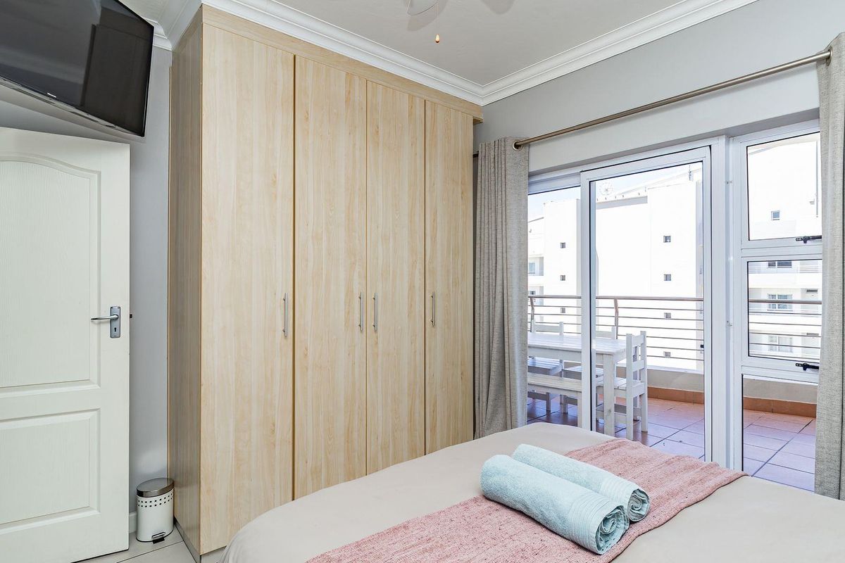 A well-maintained bedroom featuring built-in light wood cabinetry, crown molding, and sliding glass doors providing access to a private balcony.