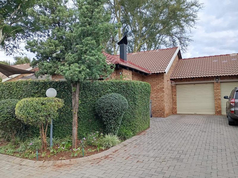 Front view of a brick townhouse featuring a double garage, paved driveway, and well-maintained garden hedge.