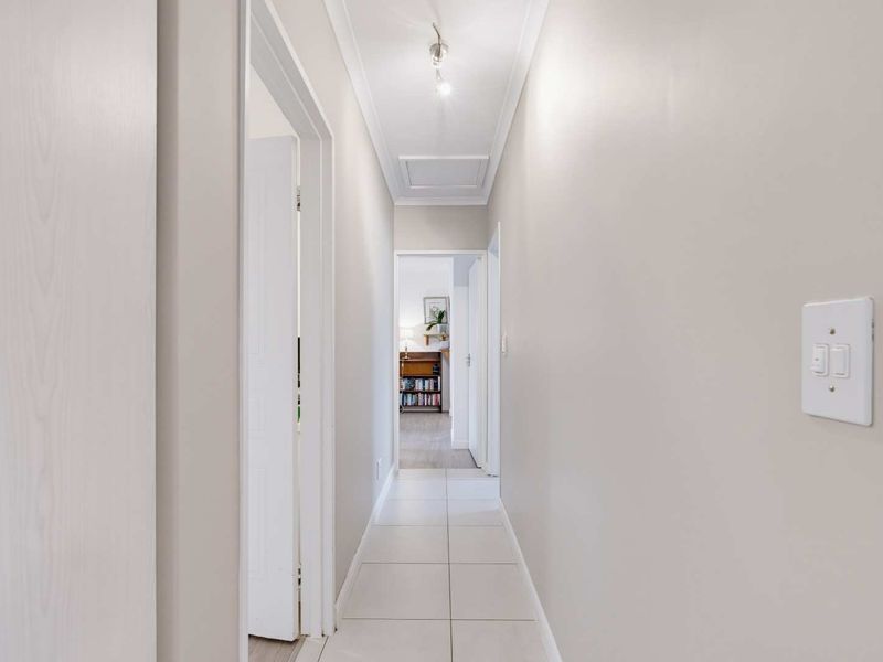 A clean, well-lit hallway featuring neutral tiled flooring and a ceiling access hatch, providing a bright transition between living spaces.