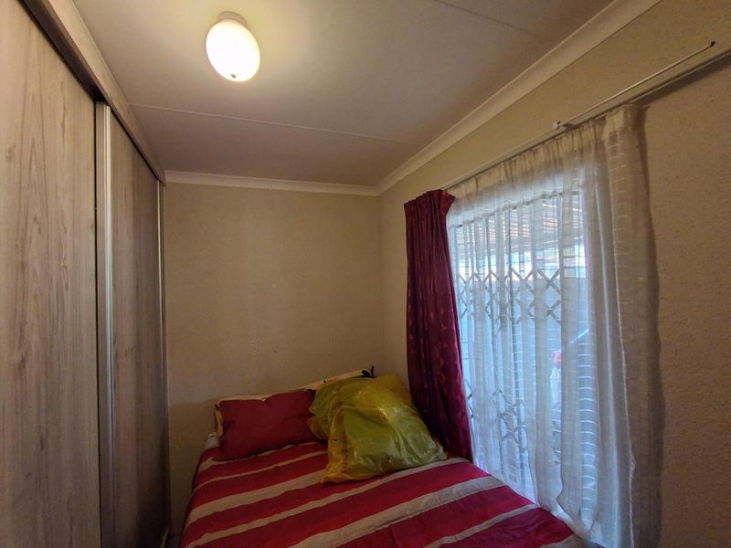 A compact bedroom featuring a built-in wardrobe, security gate on the window, and neutral wall finishes.