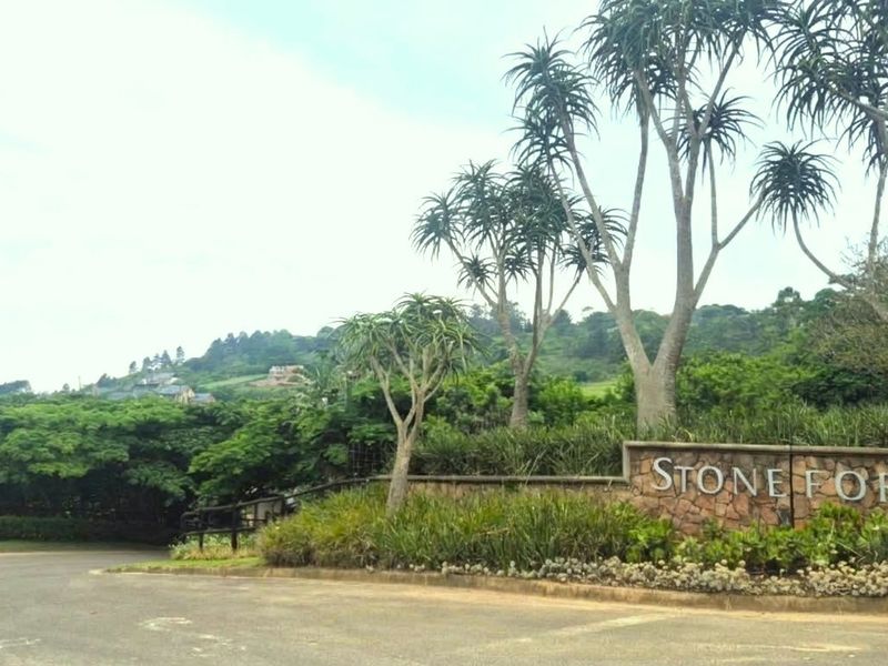 Entrance view of Stoneford estate featuring a stone signage wall, mature trees, and landscaped gardens along a paved road.