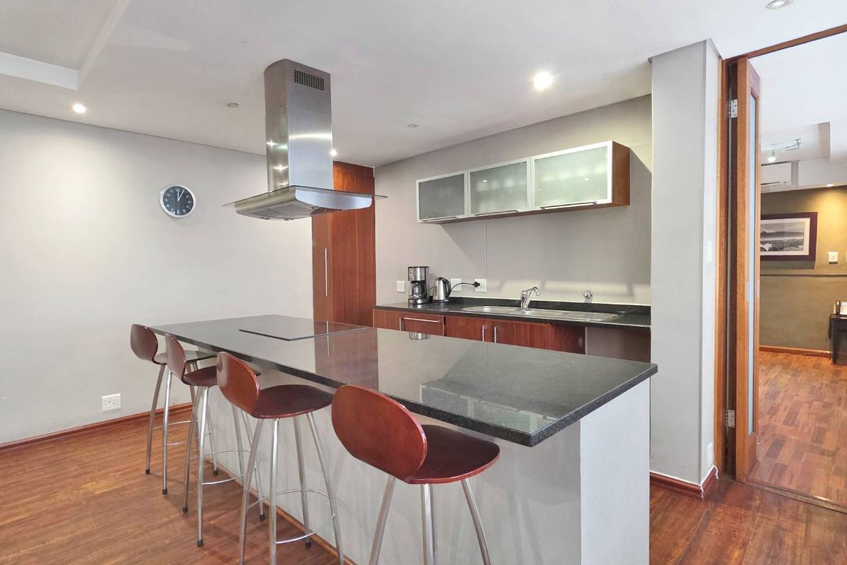 Modern kitchen featuring a central island with granite countertops, stainless steel extractor fan, and ample built-in cabinetry, finished with warm laminate flooring.