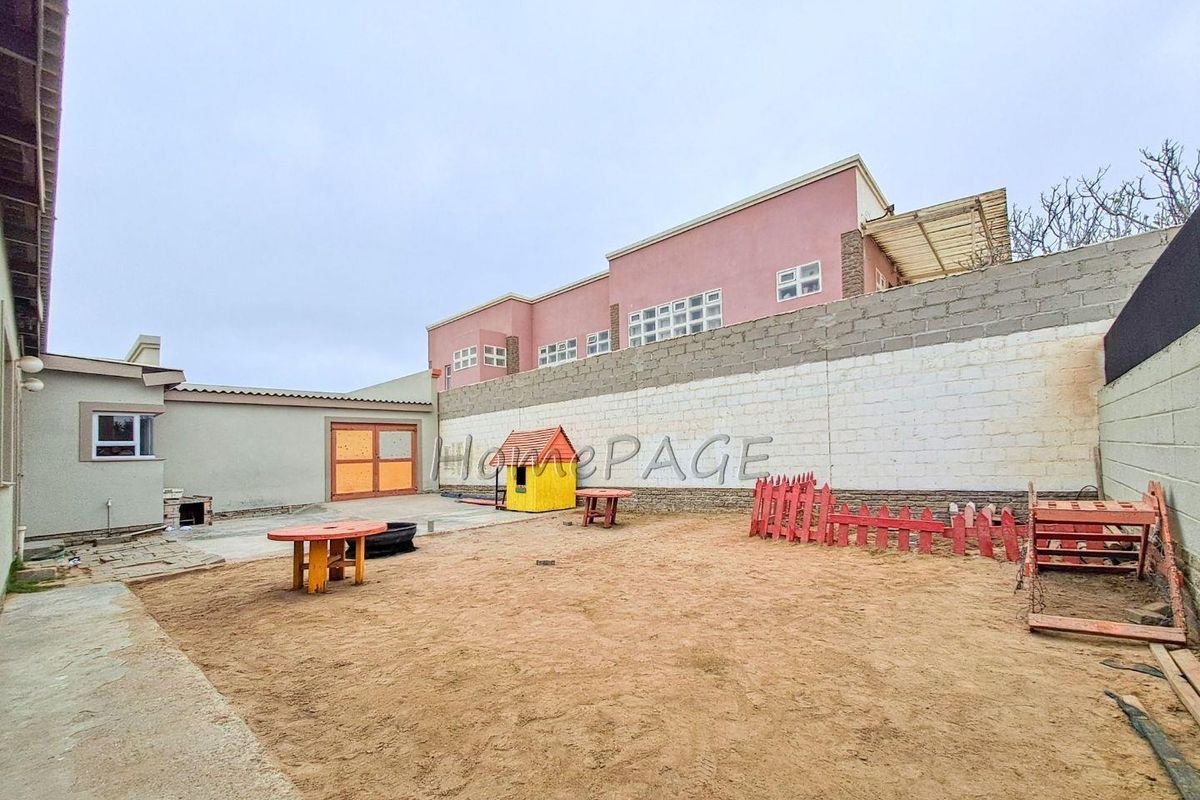 Rear exterior view of the property featuring a large sandy yard, perimeter boundary walls, and access to the main building structure.