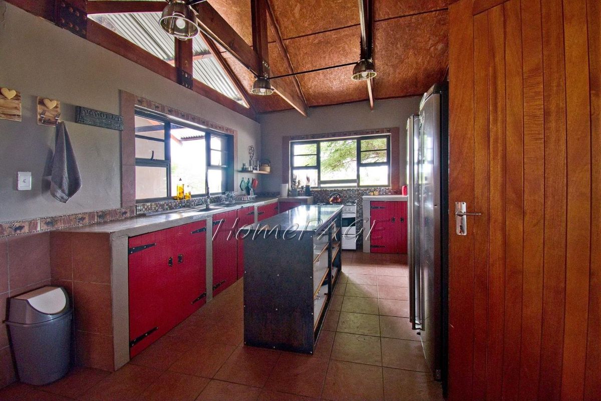 Rustic farm-style kitchen featuring exposed timber beams, tiled flooring, custom cabinetry, and a central island with integrated workspace.