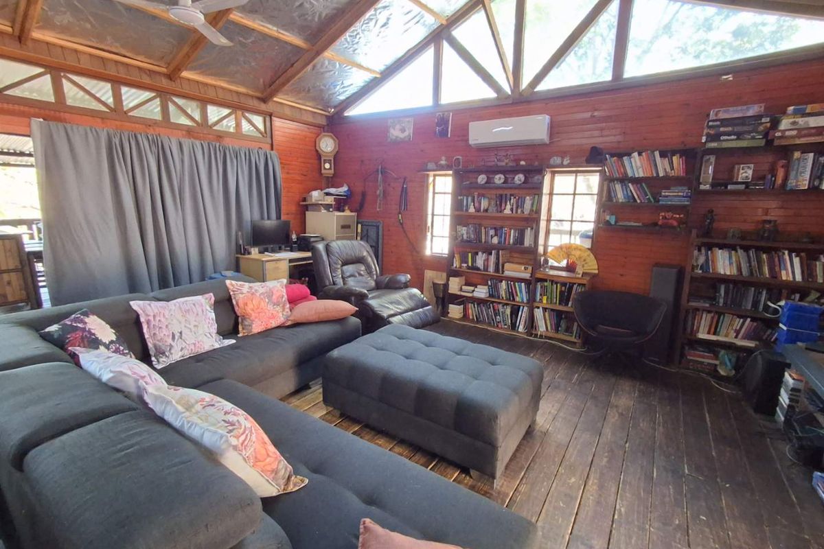 Spacious living room featuring rustic timber wall cladding, exposed roof trusses, timber flooring, and built-in shelving, creating a warm and character-filled atmosphere.