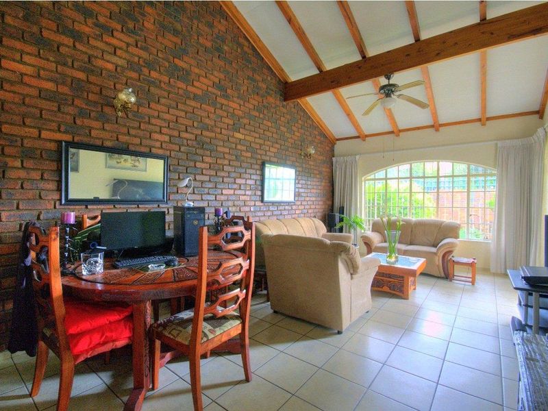 Spacious living room featuring a striking exposed brick feature wall, vaulted ceilings with timber beams, tiled flooring, and a large arched window.