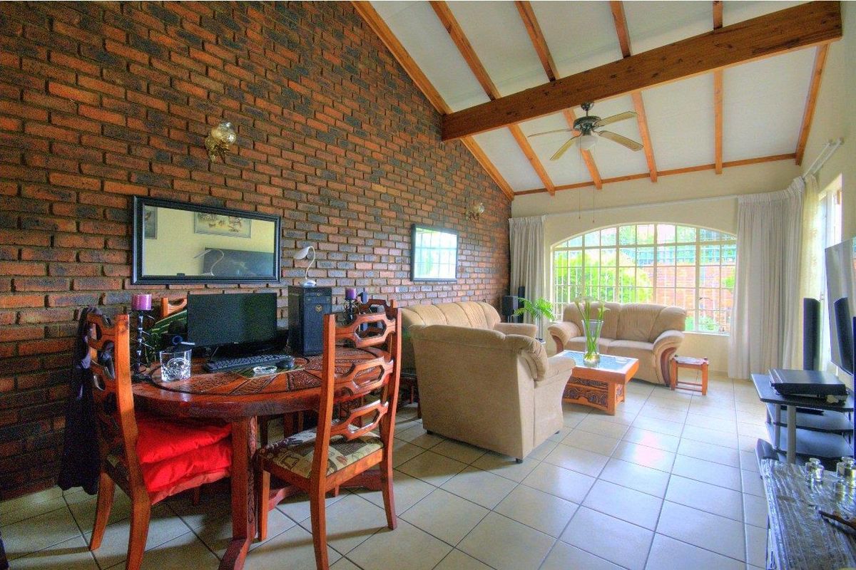 Spacious living room featuring a striking exposed brick feature wall, vaulted ceilings with timber beams, tiled flooring, and a large arched window.