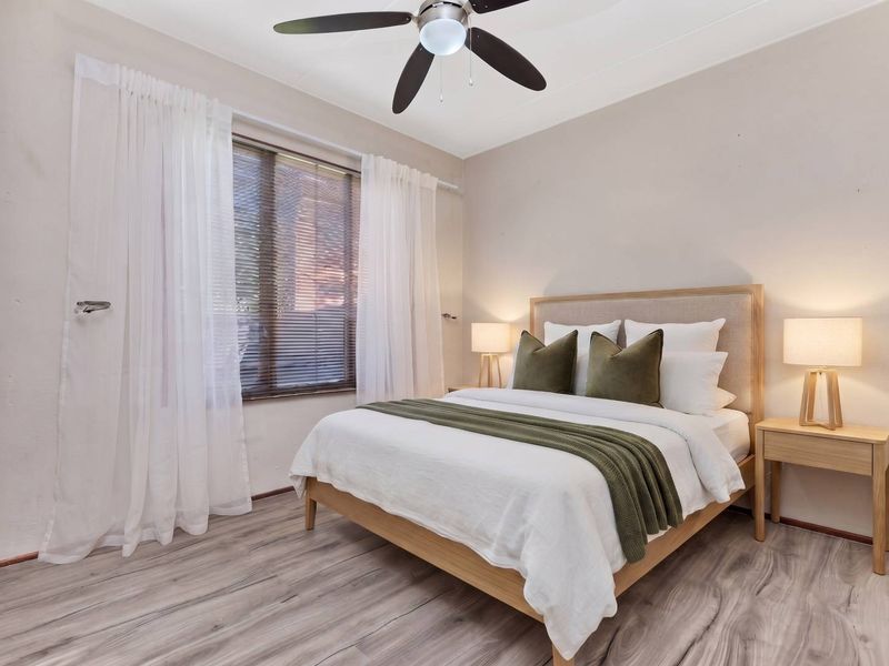 A well-maintained bedroom featuring modern laminate flooring, a ceiling fan, and large windows with venetian blinds for natural light control.