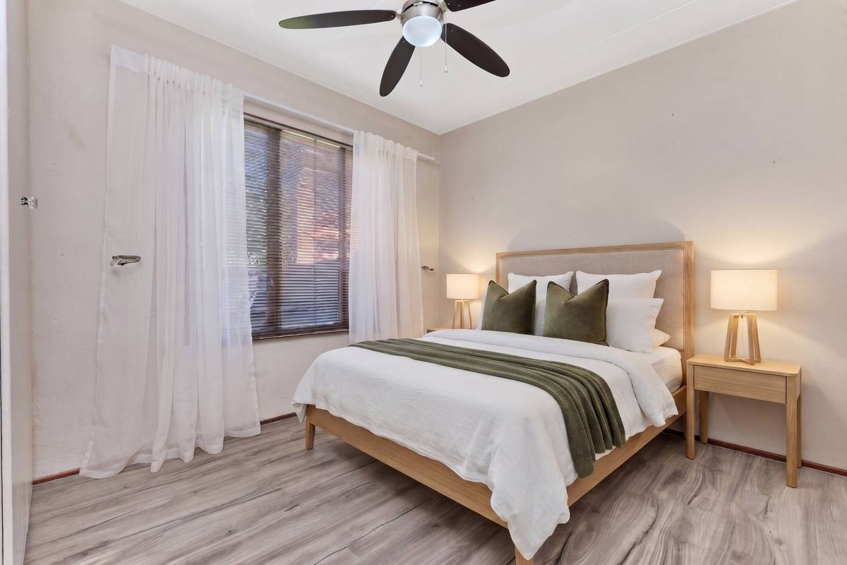 A well-maintained bedroom featuring modern laminate flooring, a ceiling fan, and large windows with venetian blinds for natural light control.