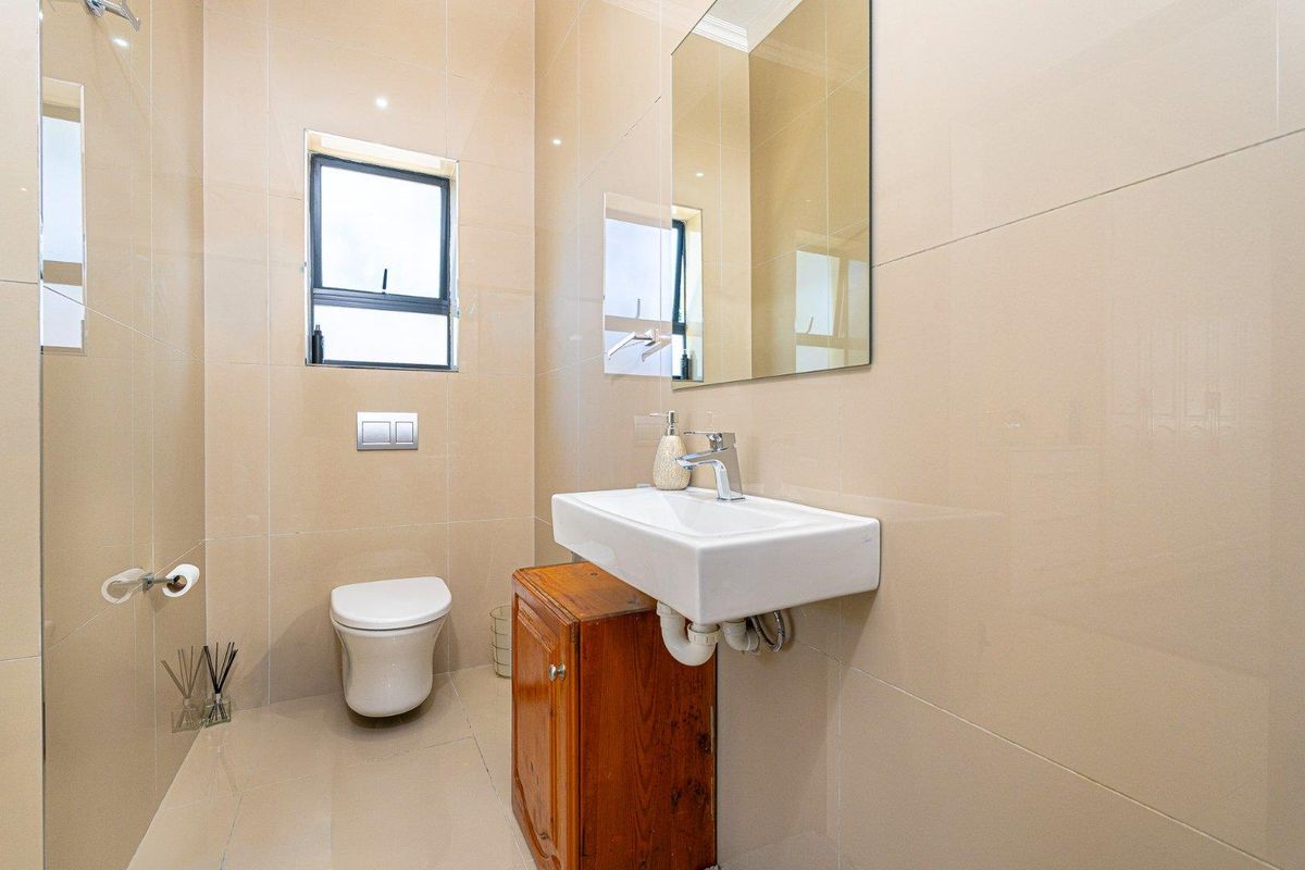 A modern bathroom featuring floor-to-ceiling beige tiling, a wall-mounted toilet, a floating basin with a wooden vanity cabinet, and a large wall mirror.