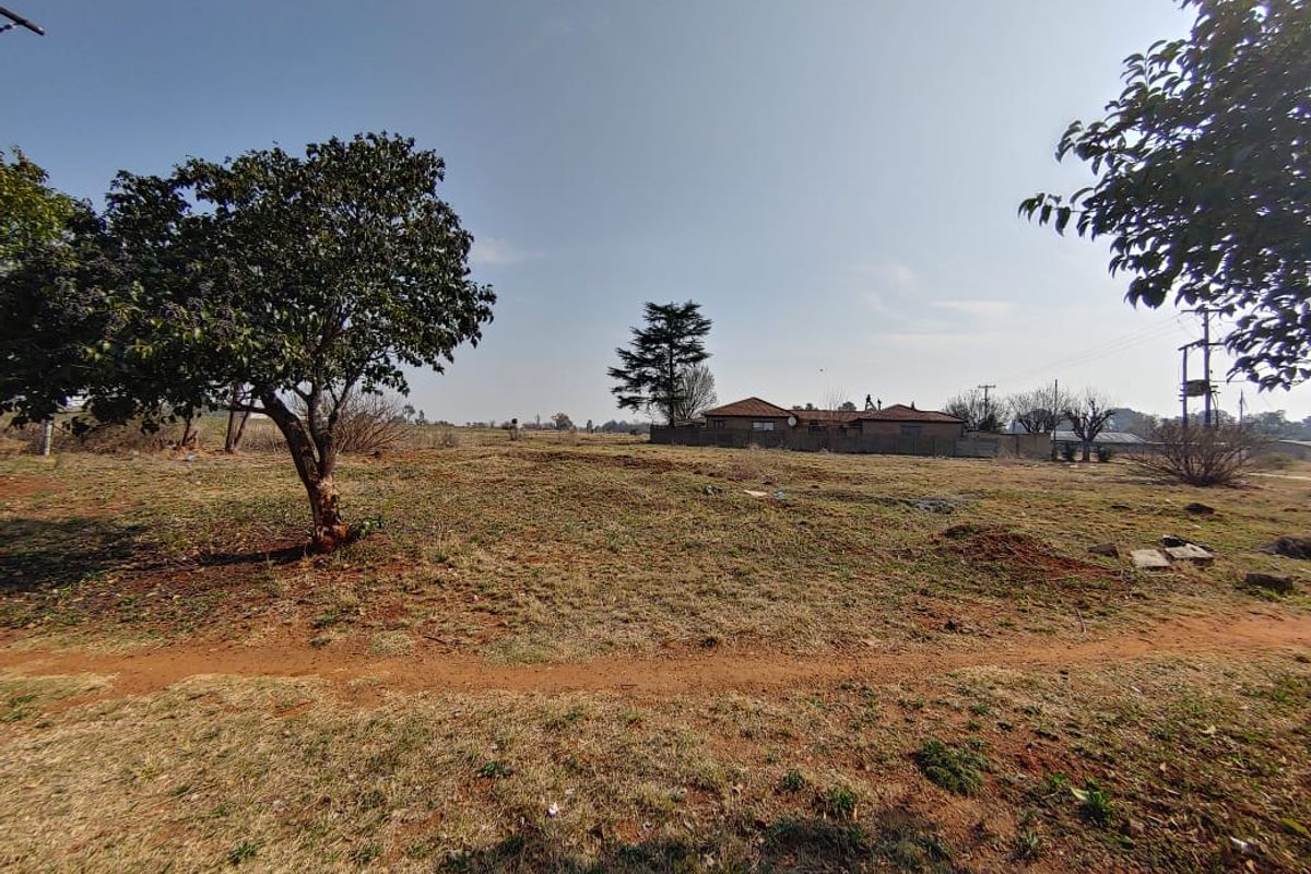 A view of a vacant residential plot featuring open grass land and mature trees, suitable for future development.