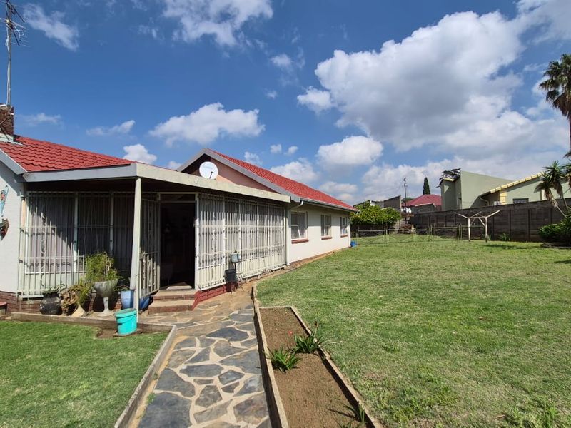 Rear view of the house featuring a covered patio, stone walkway, and a spacious garden with a boundary wall.