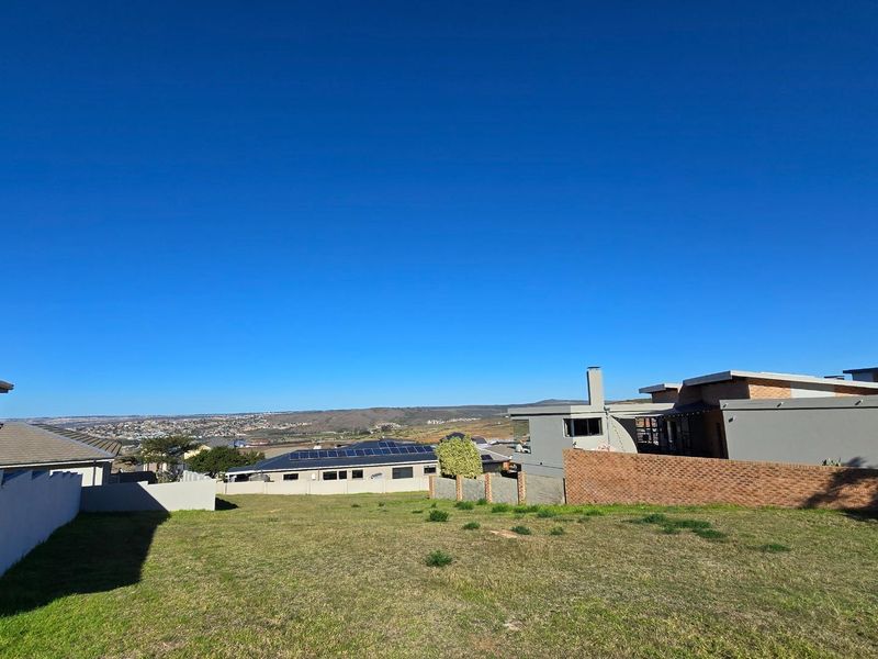 A vacant residential plot featuring a gentle slope, clear boundaries, and expansive views of the surrounding landscape and neighboring properties.