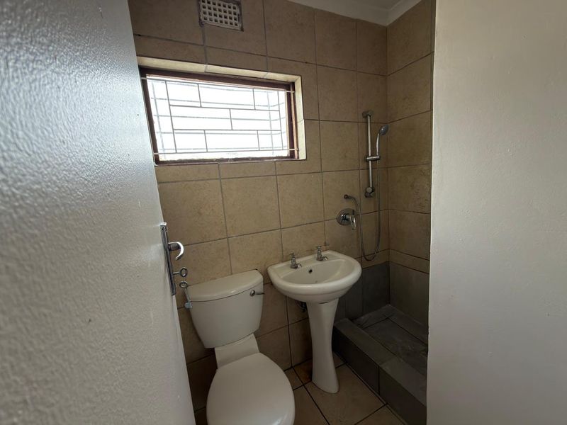 A compact bathroom featuring a pedestal basin, toilet, and shower area with tiled finishes and a small window with security bars.
