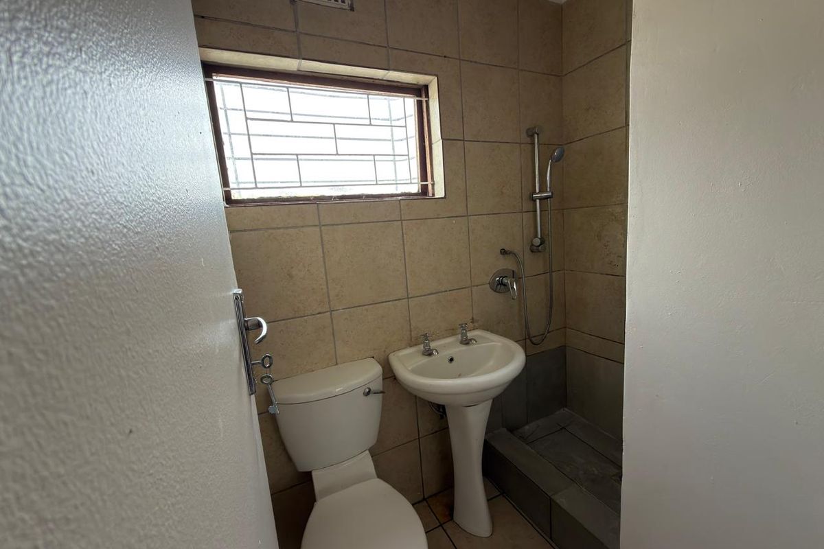 A compact bathroom featuring a pedestal basin, toilet, and shower area with tiled finishes and a small window with security bars.