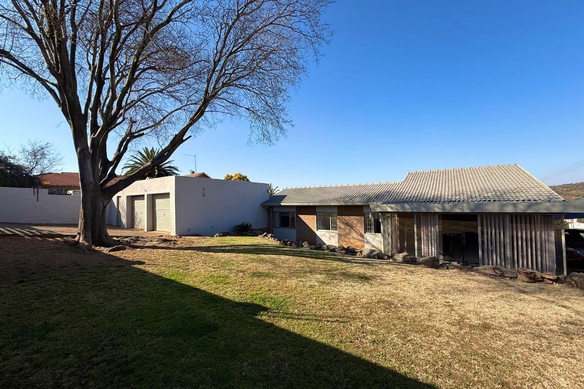 Rear view of the property featuring a spacious lawn, brick exterior, tiled roof, and a detached garage structure.