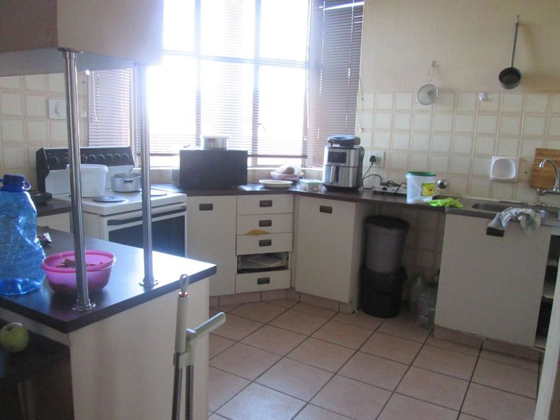 A functional kitchen featuring tiled flooring, a tiled backsplash, built-in cabinetry with laminate countertops, and a large window with venetian blinds.