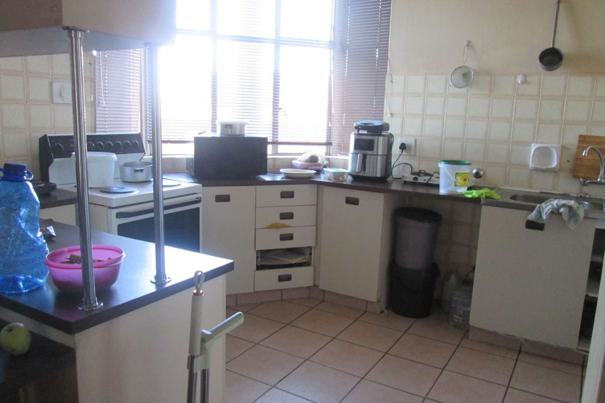 A functional kitchen featuring tiled flooring, a tiled backsplash, built-in cabinetry with laminate countertops, and a large window with venetian blinds.