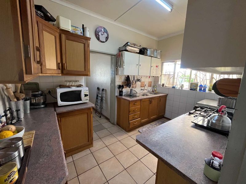 A functional kitchen featuring wooden cabinetry, laminate countertops, a double bowl sink, and a gas hob, offering potential for modernization.