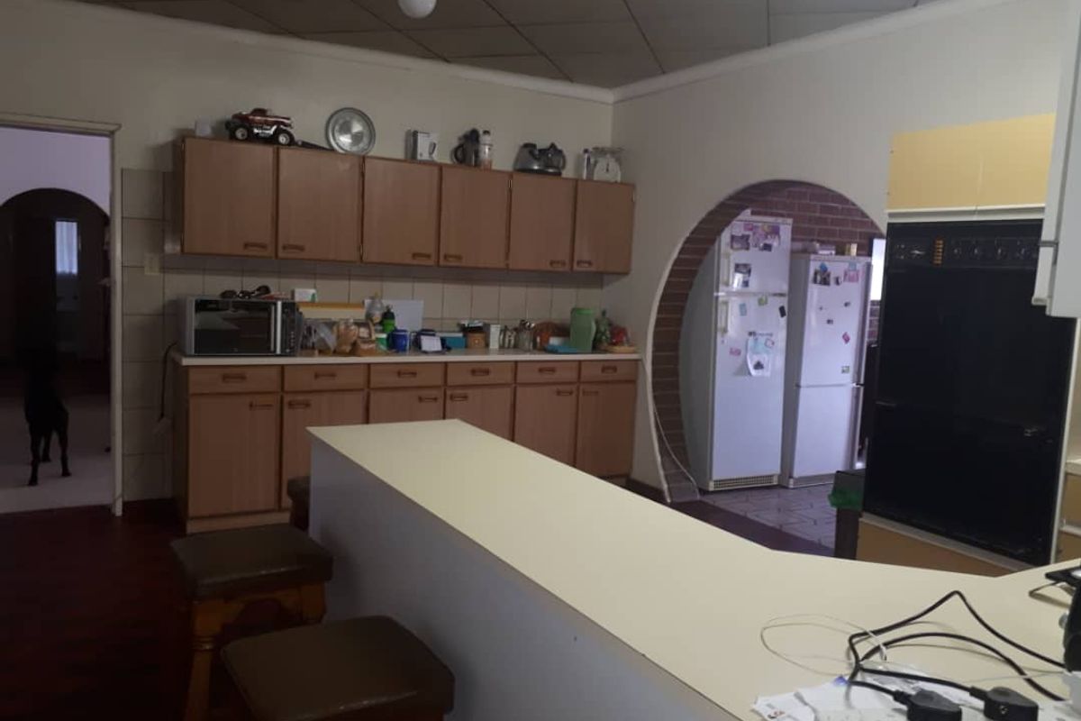 A dated kitchen featuring wood-finish cabinetry, a breakfast bar counter, and a built-in oven, with an arched doorway leading to an adjacent utility area.