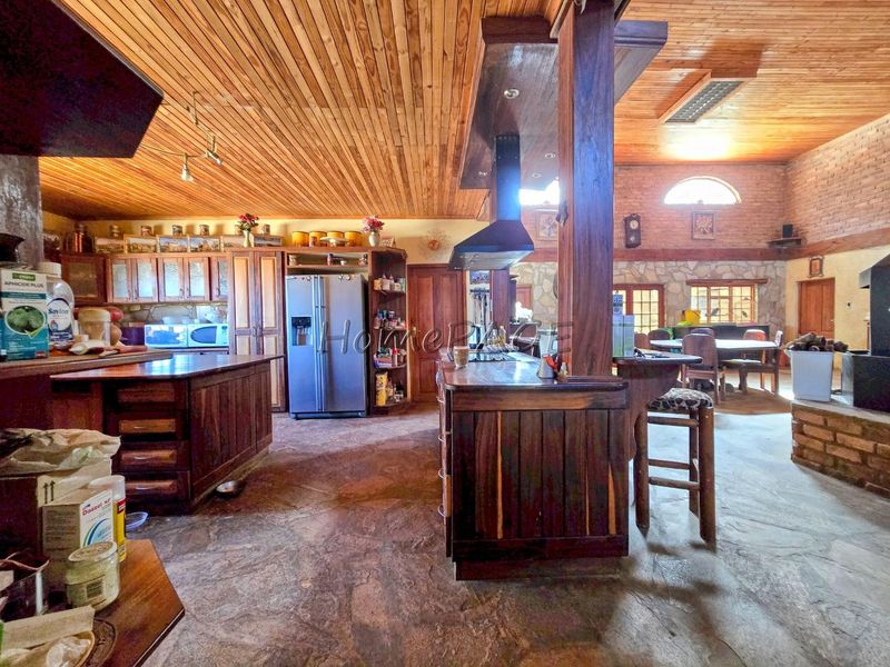 Spacious open-plan living and kitchen area featuring rustic timber ceilings, stone flooring, exposed brick walls, and extensive custom wooden cabinetry.