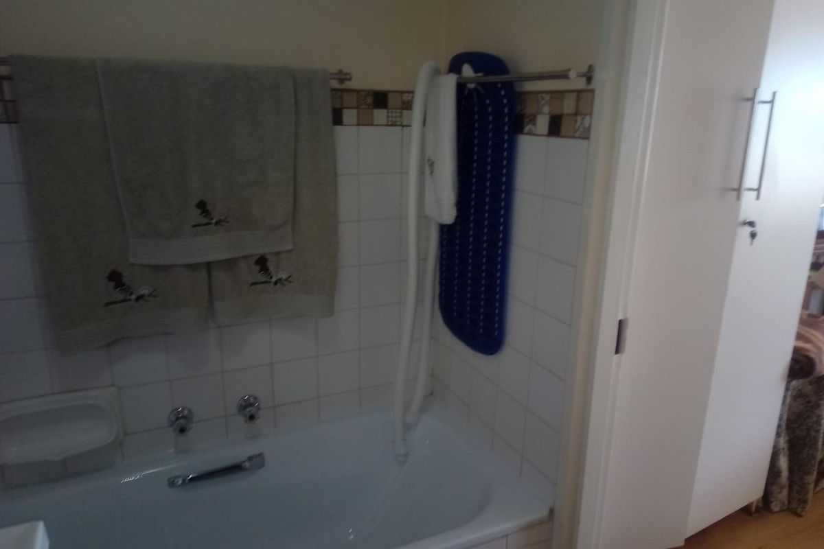 A functional bathroom featuring a standard bathtub with wall-mounted shower attachment, tiled splashbacks, and a built-in towel rail.