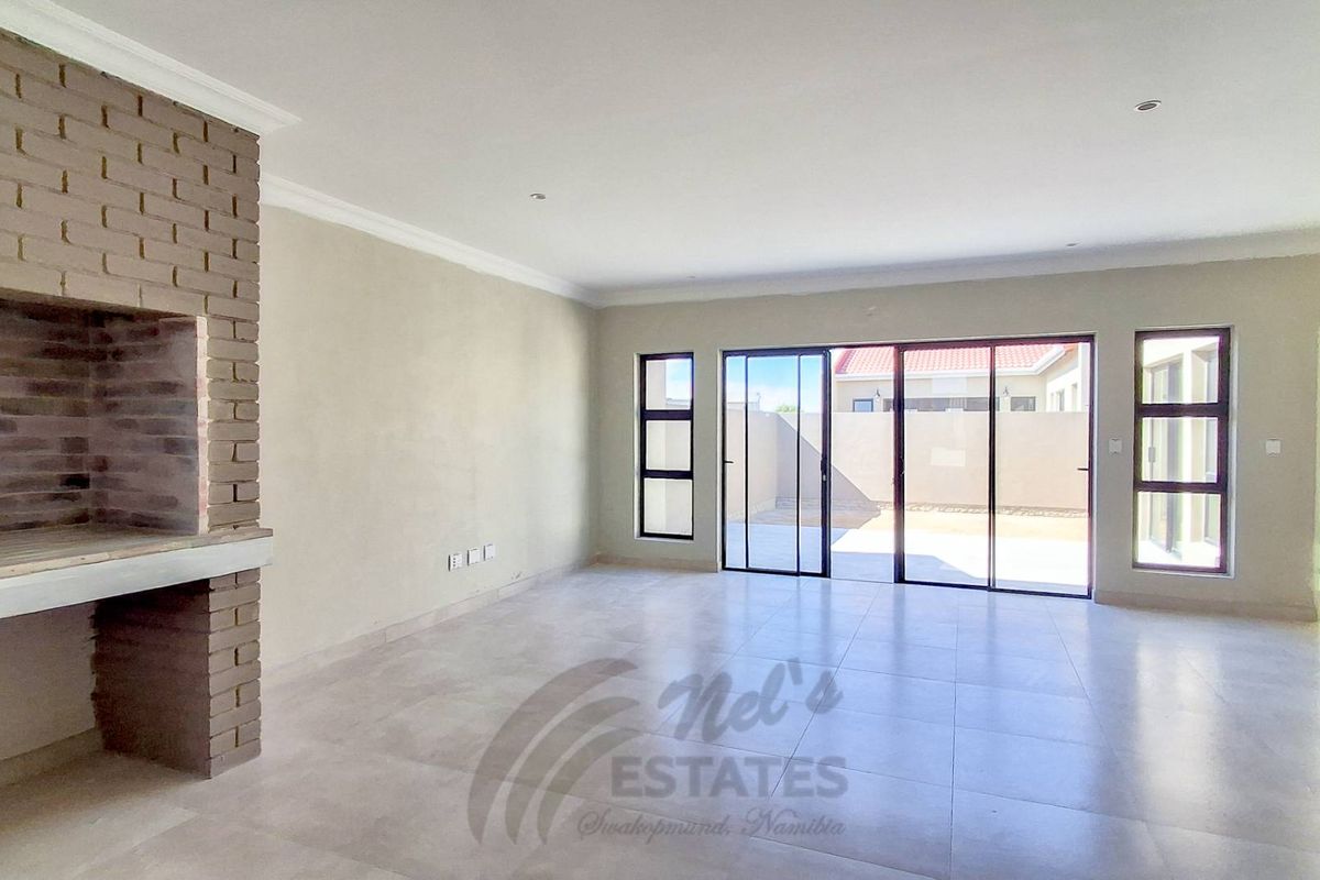 Spacious, light-filled living area featuring neutral tiled flooring, a built-in brick fireplace, and large sliding glass doors providing access to the outdoor space.