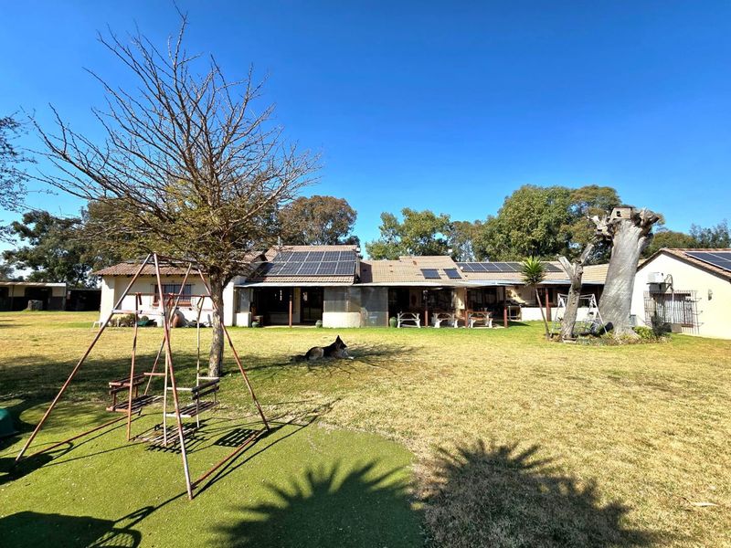 Rear view of the small holding property featuring a spacious lawn, covered patio area, and roof-mounted solar panels under a clear blue sky.