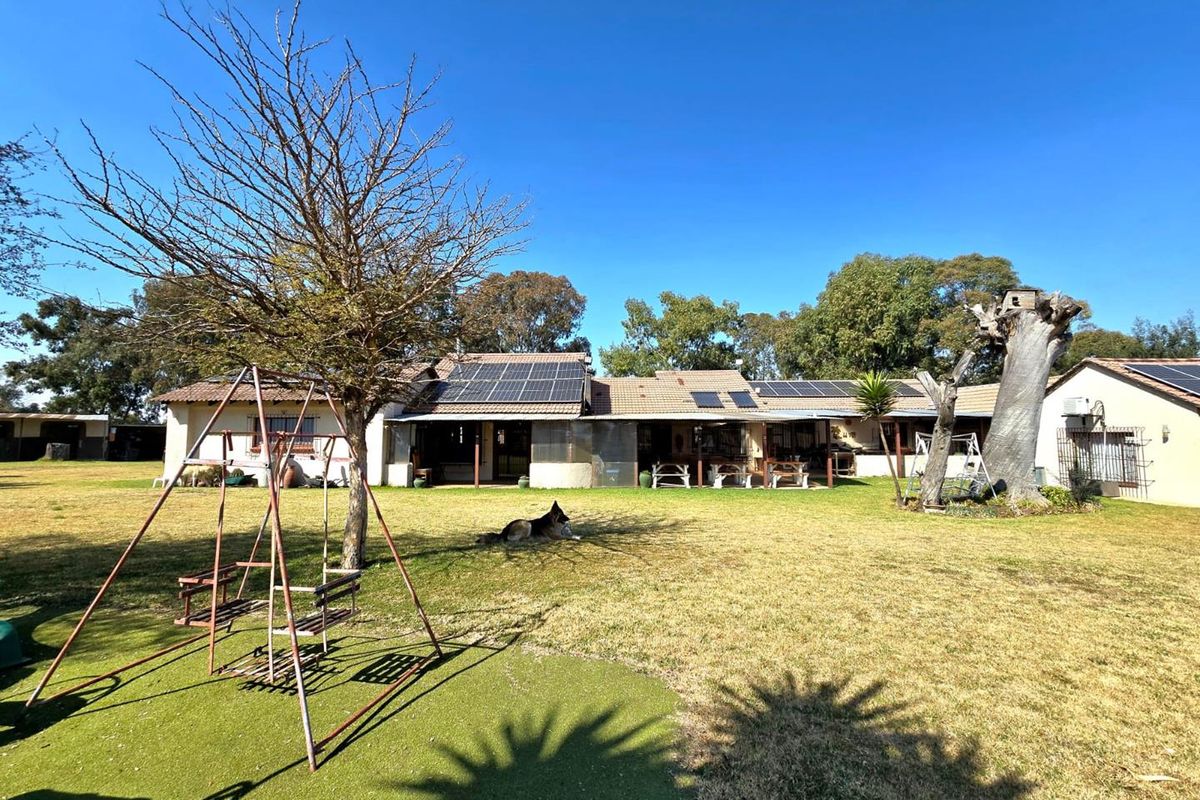 Rear view of the small holding property featuring a spacious lawn, covered patio area, and roof-mounted solar panels under a clear blue sky.