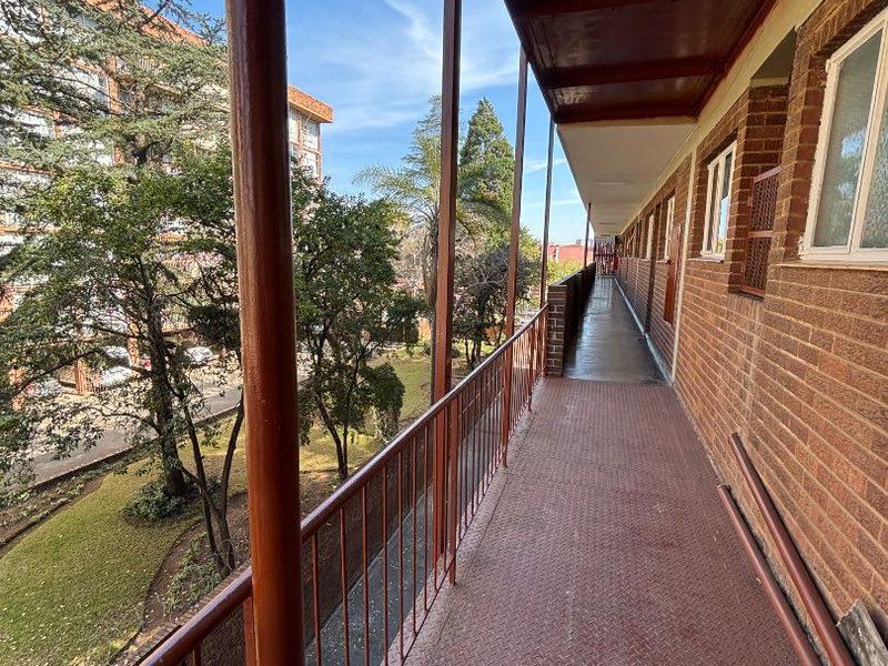 An exterior apartment balcony walkway featuring metal flooring and a metal balustrade, overlooking the surrounding grounds.