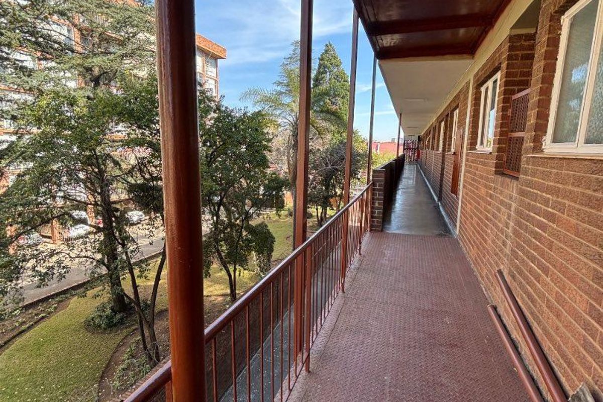 An exterior apartment balcony walkway featuring metal flooring and a metal balustrade, overlooking the surrounding grounds.